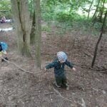 Schüler in Wald, zwei Kinder ziehen einen Ast über den Weg.