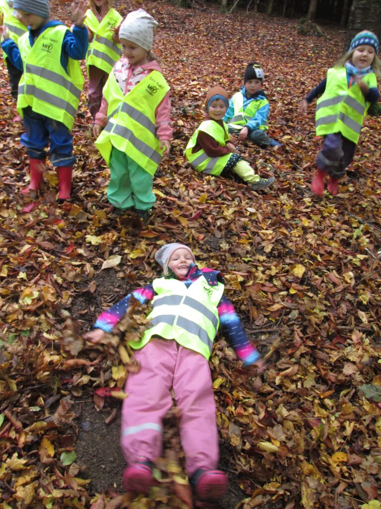 Kinder in Sicherheitswesten spielen im Herbstlaub.
